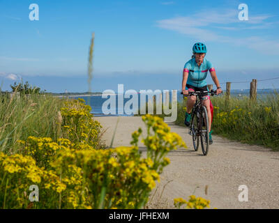 Woman riding bike on dirt track near sea Stock Photo