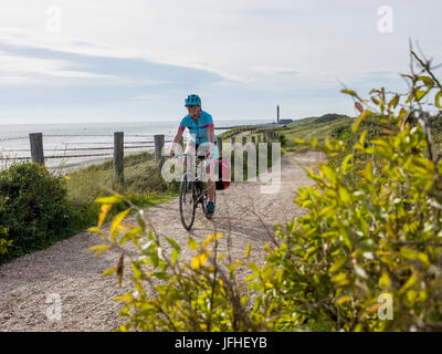 Woman riding bike on track beside sea Stock Photo