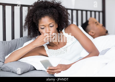 Shocked woman looking at mobile phone in bed Stock Photo