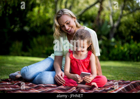 Mother looking at daughter using phone in yard Stock Photo