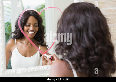Beautiful young woman drawing big heart on mirror Stock Photo
