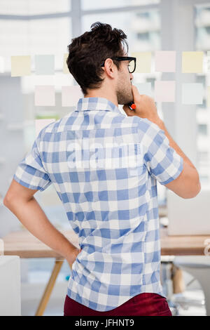 Thoughtful man reading at sticky notes on window Stock Photo