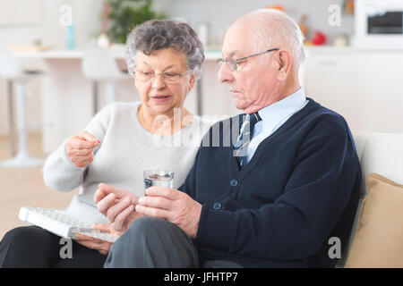 Elderly woman administering medication to husband from pillbox Stock Photo