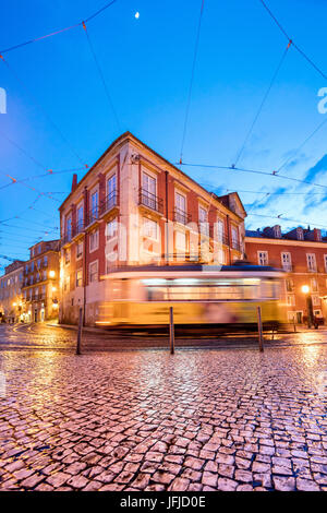 City lights on the typical architecture and old streets at dusk while the tram 28 proceeds Alfama Lisbon Portugal Europe Stock Photo