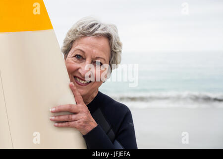 Senior woman in wetsuit holding a surfboard on the beach Stock Photo