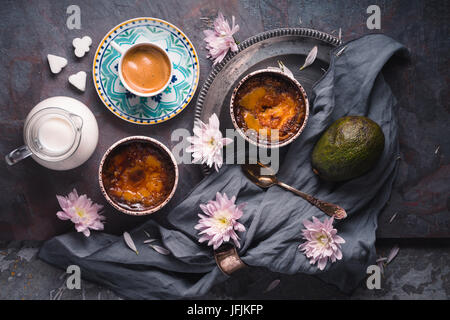 Creme brulee , cup of coffee , milk , avocado and flowers on the stone background top view Stock Photo
