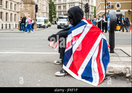 London, UK. 01st July, 2017. LONDON, ENGLAND - JULY 01 Demonstrator with black hood and mask is sitting in the middle of Whitehall with the Union Jack on his back. Thousands of protesters joined the anti-Tory demonstration on the 1st July 2017. They marched from the BBC Broadcasting House to Parliament Square. They were calling for an end to the Conservative Government and policies of austerity. Credit: onebluelight.com/Alamy Live News Credit: onebluelight.com/Alamy Live News Stock Photo