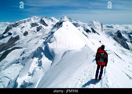 A hiker contemplating the breathtaking view from the Breithorn summit, in the Mount rosa Massif, with the Lyskamm, Castor, Pollux, on the border between Italy and Switzerland Europe Stock Photo