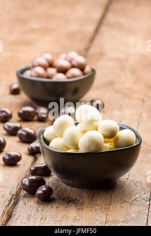 white chocolate pralines into black bowl, on wooden table Stock Photo