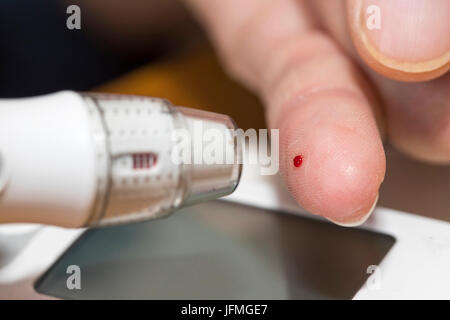 Diabetics with a blood glucose test, with a lancing device a blood drop is generated at the fingertip, for blood sugar measurement, Stock Photo