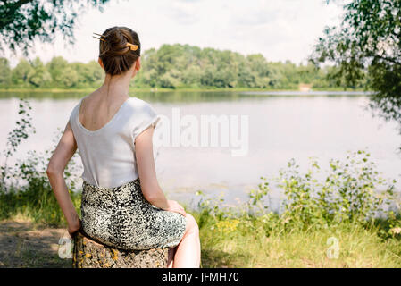 A woman is sitting close to the Dnieper river in Kiev, Ukraine, and is watching or observing far in the distance, under a warm and soft summer sun Stock Photo