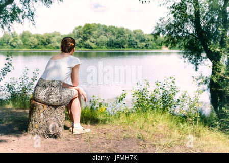 A woman is sitting close to the Dnieper river in Kiev, Ukraine. She is thinking while watching or observing far in the distance, under a warm and soft Stock Photo