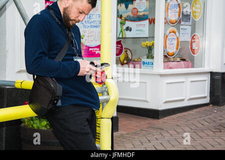 A candid shot of a young bearded man using a smartphone in a busy UK high street. Stock Photo
