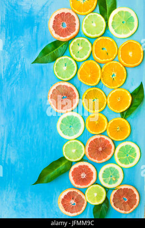 Variety of colorful sliced citrus fruits oranges, grapefruits, lemons, limes with green leaves on blue background, styled composition, abstract, flat  Stock Photo