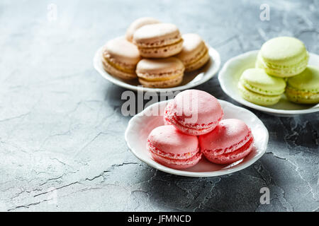 Three plates with macaroons pink, green and brown on the table Stock Photo