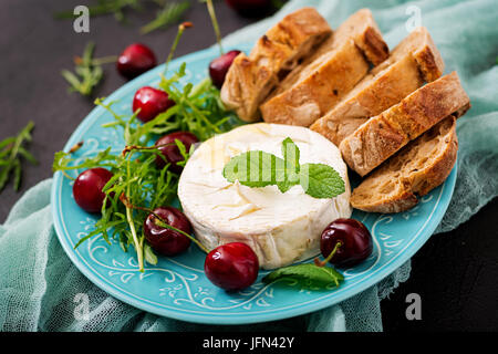Baked Camembert cheese, toast and arugula salad with  sweet cherries. Stock Photo