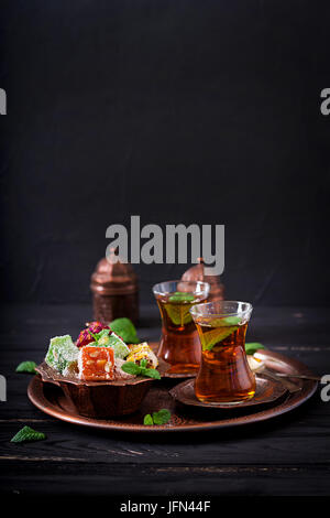 Bowl with various pieces of turkish delight lokum and black tea with mint on a dark background Stock Photo