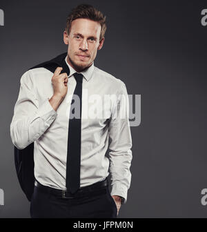 Focused young businessman standing alone in a studio against a grey background carrying his jacket over his shoulder Stock Photo