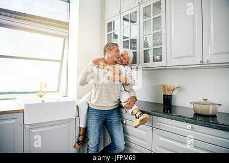 Affectionate senior couple laughing and sharing a playful moment together while relaxing in their kitchen at home Stock Photo