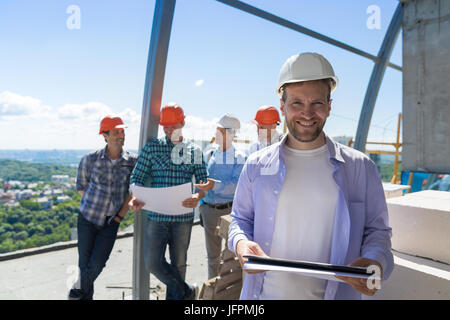 Team Of Builders On Site, Contractor Hold Plan Happy Smiling Over Apprentices Group Discussing Blueprint Stock Photo