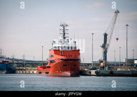 Red freight ship in front of port facilities and cranes Stock Photo