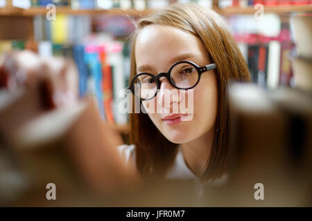 People: young girl, student, wearing eyeglasses, chooses a book in a library or bookstore, smiling. Stock Photo