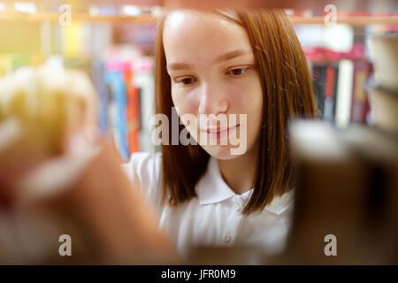 People: young girl, student, chooses a book in a library or bookstore, smiling, sunlight effect. Stock Photo