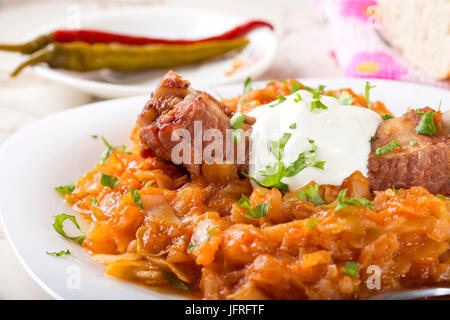 Cabbage stew with Smoked Pork Ribs, cream and green parsley Served in white plate with pickled chili peppers Stock Photo