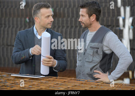 two male architects discussing a blueprint outdoors Stock Photo