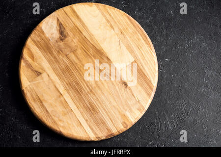 Rustic wooden round cutting board on black stone background close up - empty pizza cutting board, copy space for text, design element Stock Photo