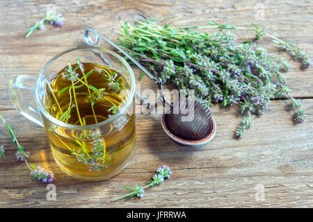 Healthy herbal tea with bunch of fresh wild thyme and vintage tea-strainer on old wooden background. Cup of thyme tea, herbal drink. Stock Photo