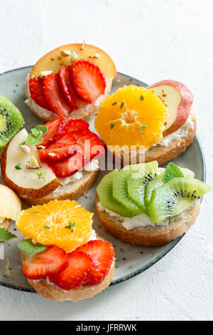 Fruit dessert sandwiches with ricotta cheese. Delicious healthy breakfast toasts with cream cheese, fresh organic fruits and berries, herbs, nuts and  Stock Photo