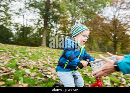 Little boy driving with his walking bicycle towards arms of mother in autumn scenery Stock Photo