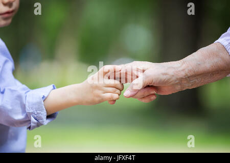 Cropped view of young boy holding great grandmother's hand outdoors Stock Photo