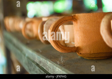 Handmade baked clay cups on wooden shelves in pottery workshop waiting for glazing process. Selective focus. Narrow depth of field. Stock Photo