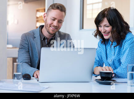Two smiling young coworkers using a laptop in an office Stock Photo