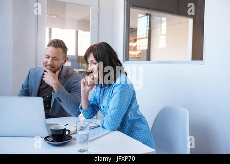 Two smiling businesspeople working on a laptop in an office Stock Photo