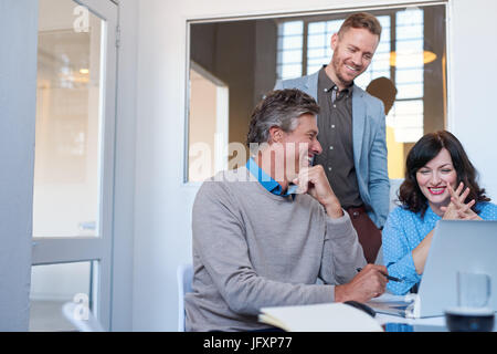Smiling office coworkers talking together while using a laptop  Stock Photo
