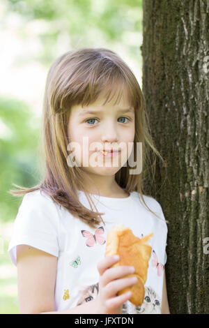 Cute little girl with big blue eyes enjoys eating her favorite croissant Stock Photo
