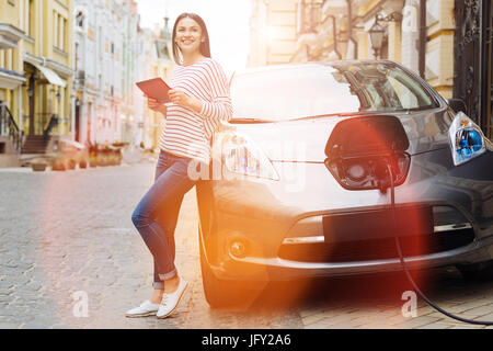 Young woman using tablet while charging the car Stock Photo