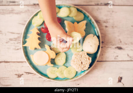 Creative idea for child food. Funny breakfast. Children's hand holds cucumber. Sandwiches in the shape of a bunny, butterfly, tree. Concept of healthy Stock Photo