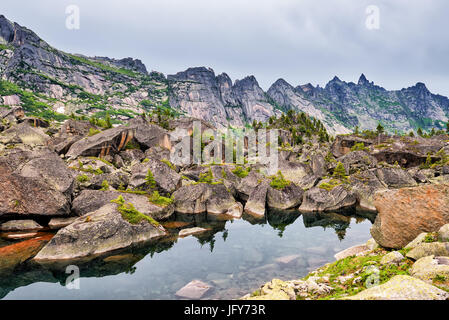Small mountain lake in glacial moraine from large boulders. Ergaki Ridge. Western Sayan. Central Asia Stock Photo