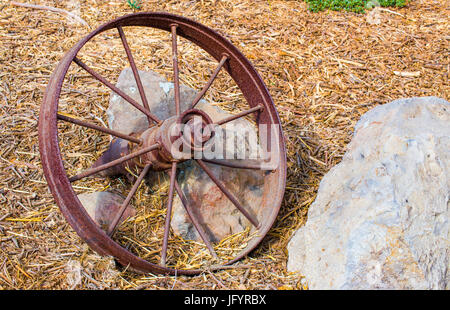 weathered rusting wagon wheel against rock on ground Stock Photo