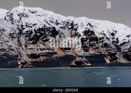 A snow-capped mountain with ice floes floating by from a blue tidewater glacier. Stock Photo