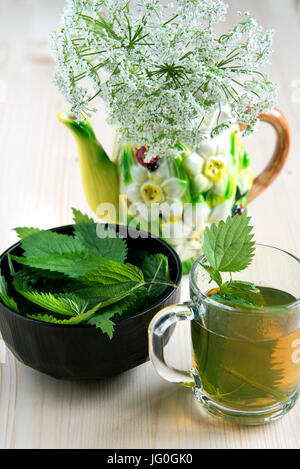 Nettle tea on the wood background leaves in the cup on a wooden table and wild flowers Stock Photo