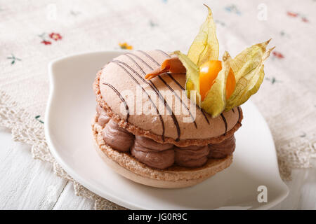 Elegant dessert: macaroon with chocolate cream decorated with physalis close-up on a plate. horizontal