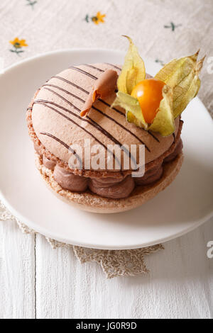 Beige delicious macaroon with chocolate cream decorated cape gooseberry close-up on a plate. vertical Stock Photo