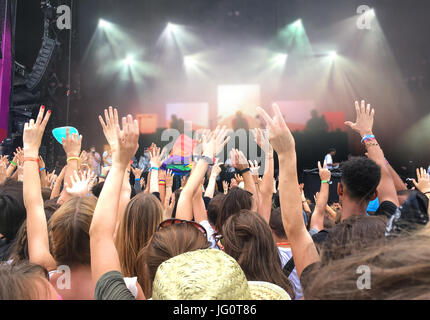 Audience with hands raised at a music festival, blurred stage lights in the background Stock Photo