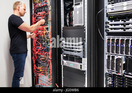Side view of mid adult male IT consultant checking with network cables connected to servers in datacenter Stock Photo