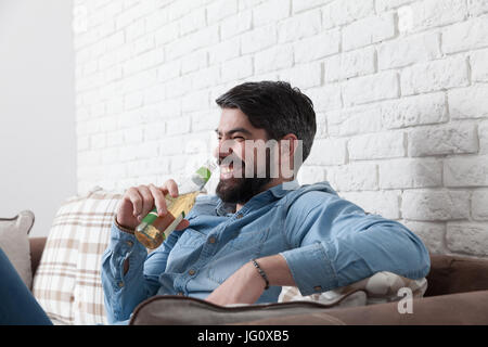 Handsome man sitting relaxed on a sofa while is drinking a beer. Stock Photo